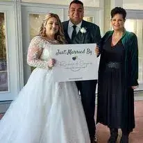 Newlyweds with officiant holding a “Just Married” sign outside a venue