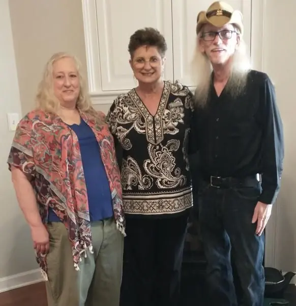 Three people posing indoors; two women and one person in black with a cowboy hat, smiling.
