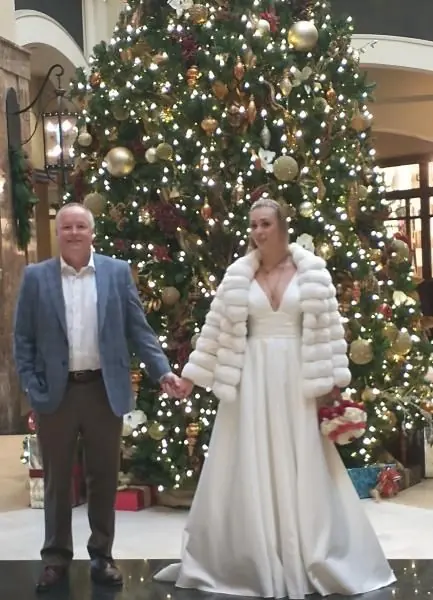 Couple holding hands in front of a large decorated Christmas tree in a lobby
