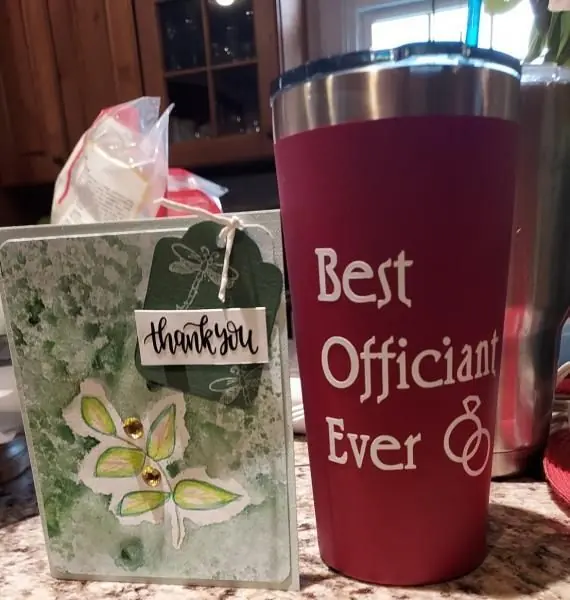 Thank-you gift bag and maroon tumbler reading “Best Officiant Ever” on a kitchen counter
