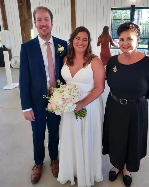 Three people dressed for a wedding, with the bride holding a bouquet indoors.
