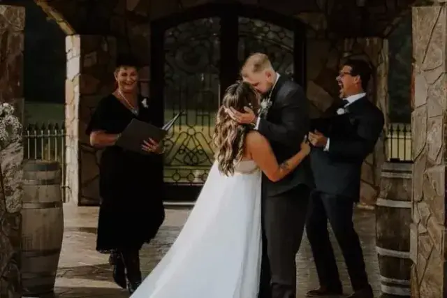 Wedding couple kissing beside an officiant and best man under a stone archway