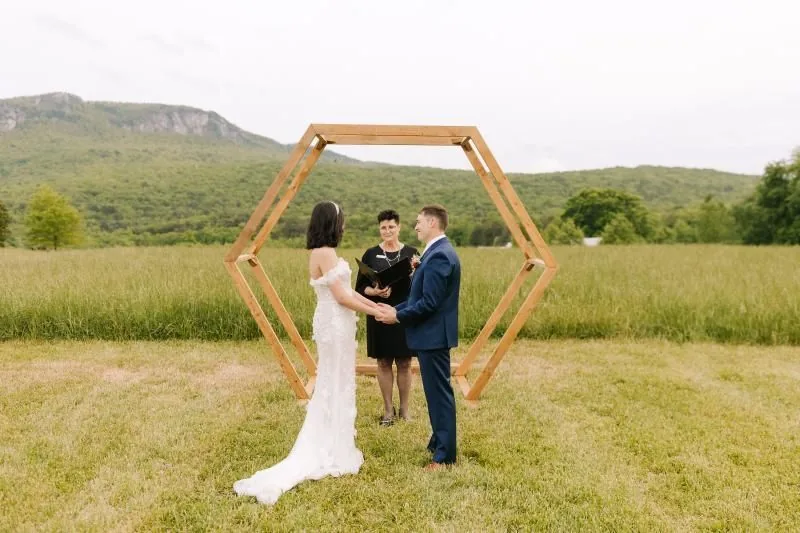 Couple under a wooden hexagon arch in a mountain meadow