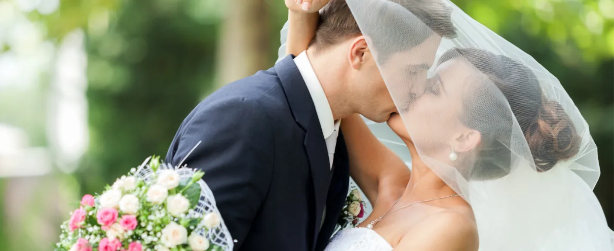 Bride and groom kissing outdoors with a bouquet in the foreground